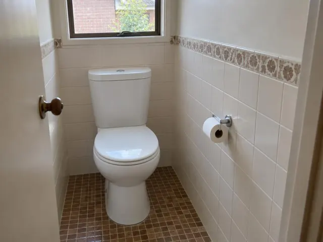 Clean white toilet in a tiled bathroom with window and tiled floor in Menai