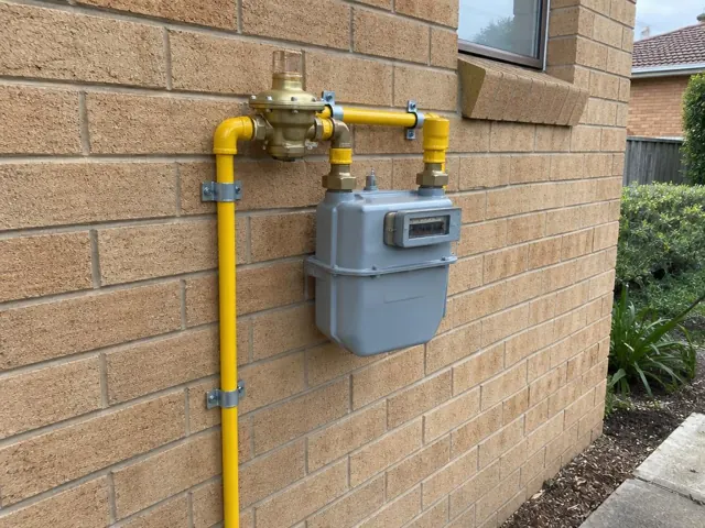 Gas meter and yellow pipe fittings on a brick house wall with a window in Illawong